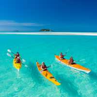 Whitsundays kayakers paddle across turquoise water toward a sandy cay, Queensland.