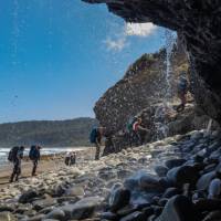 Trekking behind a waterfall on the South Coast Track | John Dalton