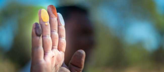 An Indigenous guide shows black, yellow, orange and white ochres during a cultural tour experience | Tourism NT/Matt Glastonbury